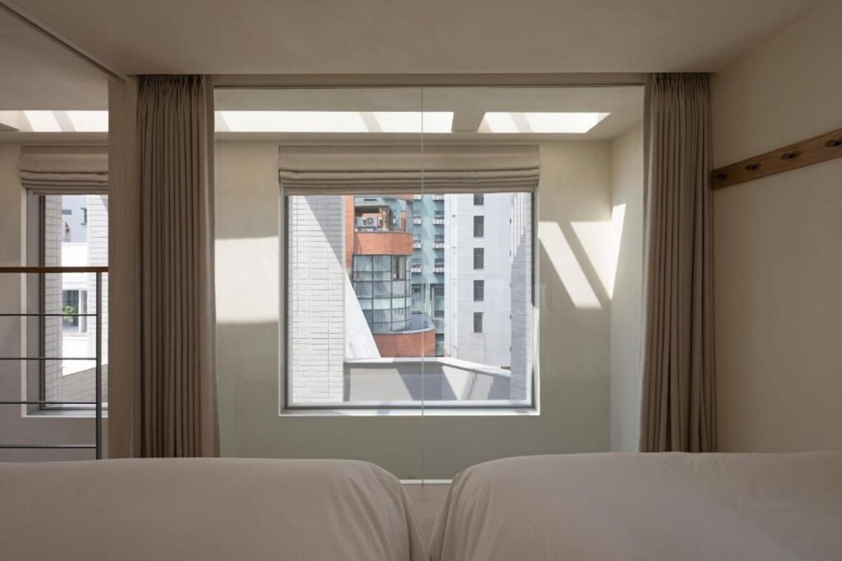 Quarto de hotel com uma janela grande, uma cama e cortinas.