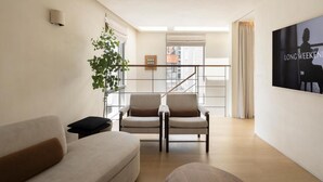 Una sala de estar moderna con un sofá, dos sillones, una mesita auxiliar, una planta y un cuadro en la pared.