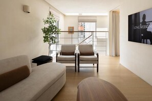 Uma sala de estar moderna com um sofá, duas poltronas, uma mesa lateral, uma planta e um quadro na parede.