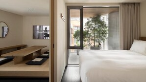 Una habitación de hotel con cama, un banco, una planta en maceta y vistas al exterior.