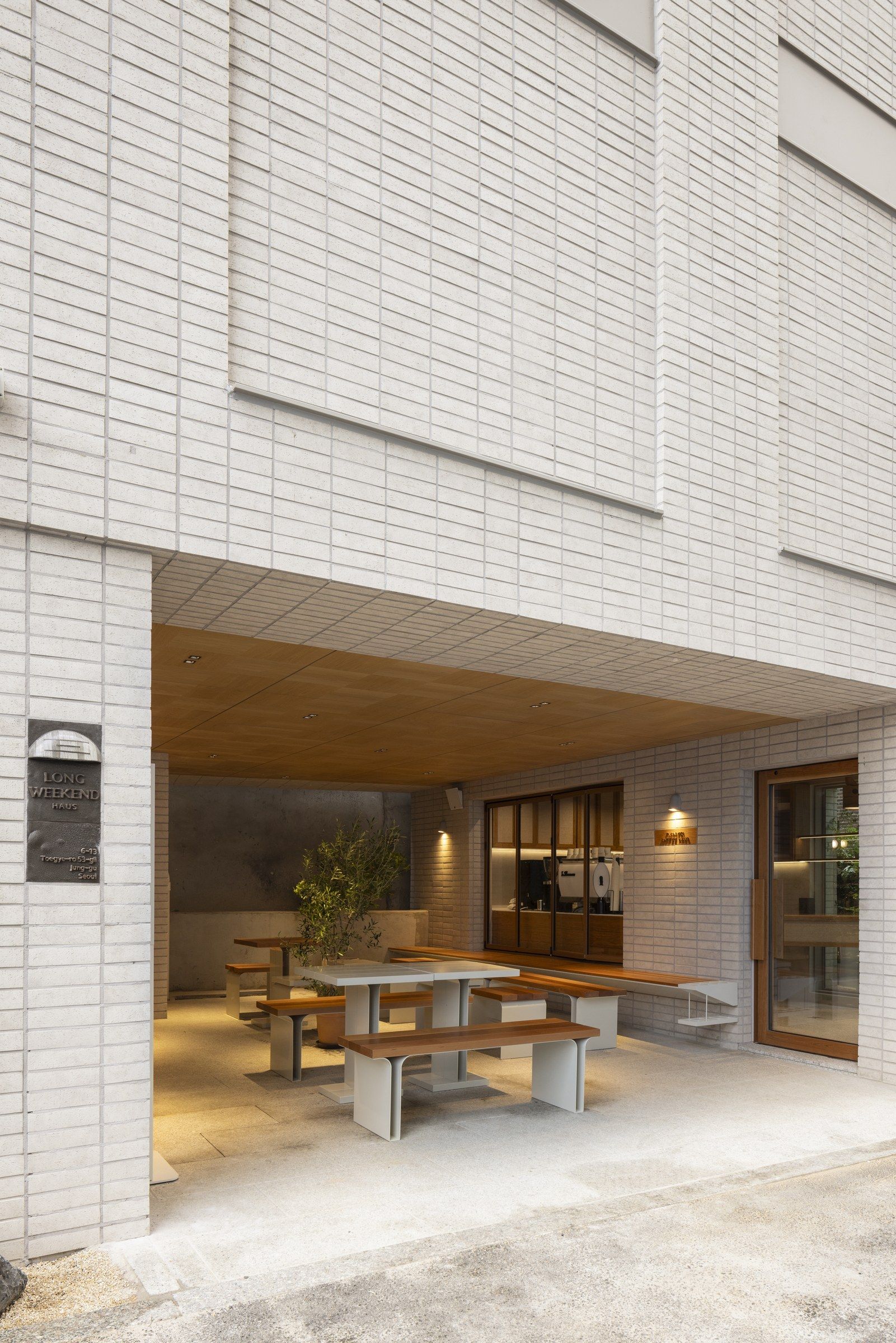 A building with a covered outdoor seating area, a sign reading 'LONG WEEKEND HAUS', and a visible entrance.