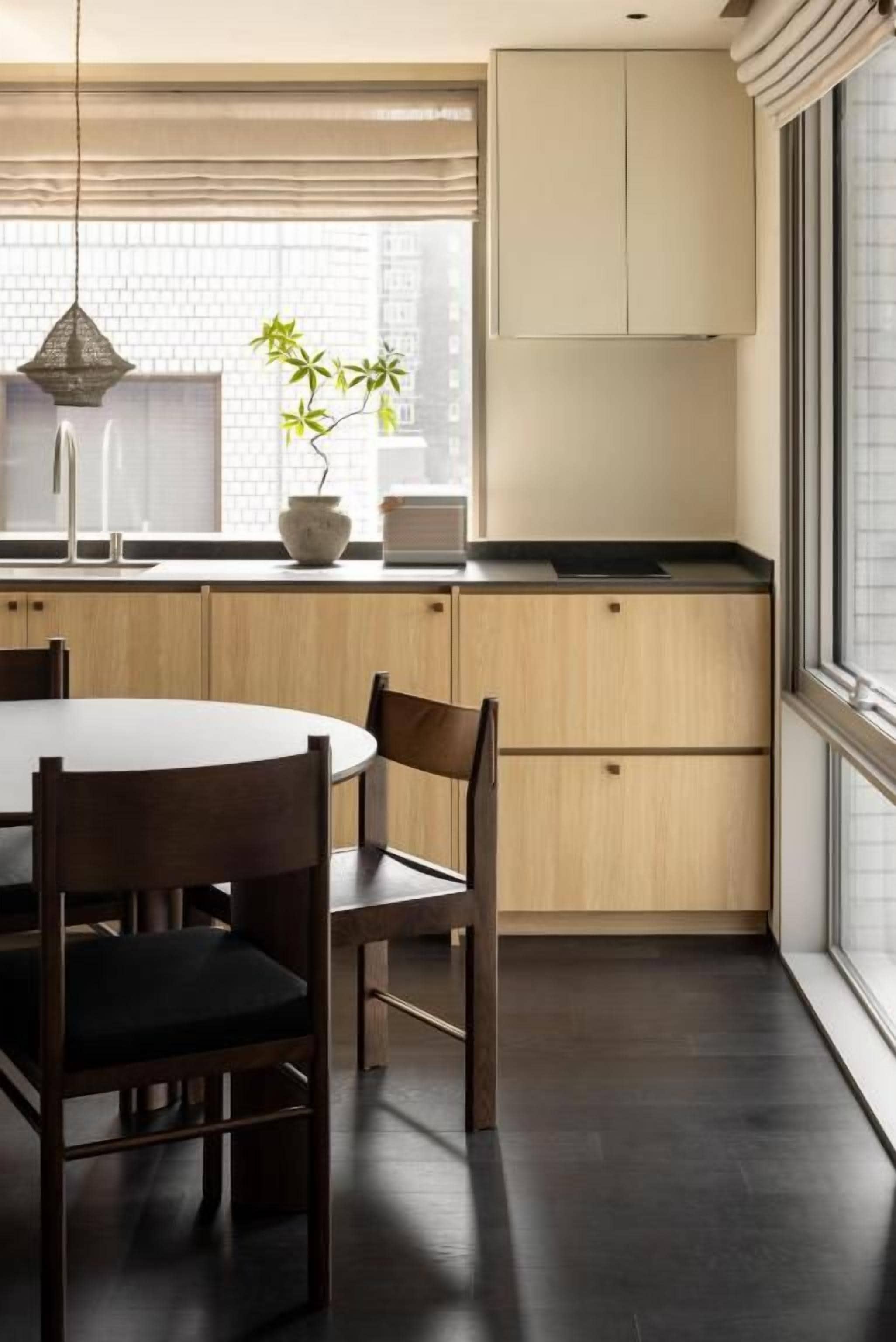 A modern kitchen with a dining table and chairs, a potted plant, and a window with blinds.
