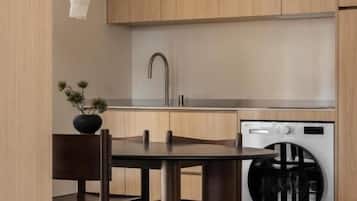 A modern kitchen with wooden cabinets, a sink, a washing machine, and a dining table with chairs.