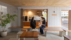 Un café con mesas y bancos de madera, una zona de estar y una barra con una máquina de café.