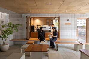Um café com mesas e bancos de madeira, área de estar e balcão com máquina de café.