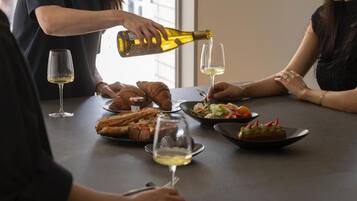 A dining table with food and wine glasses, a bottle being poured, and a person pouring wine.