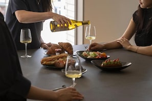 A dining table with food and wine glasses, a bottle being poured, and a person pouring wine.