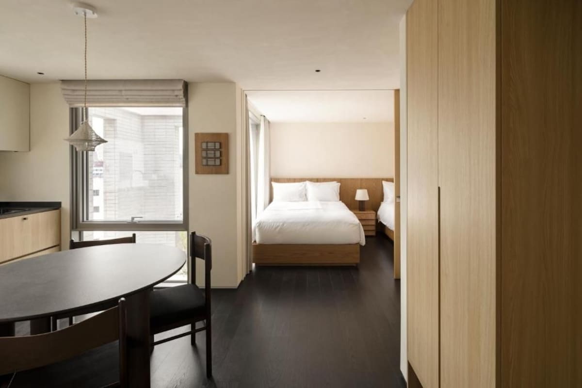 Quarto de hotel com cama, mesa de cabeceira e janela com persianas.