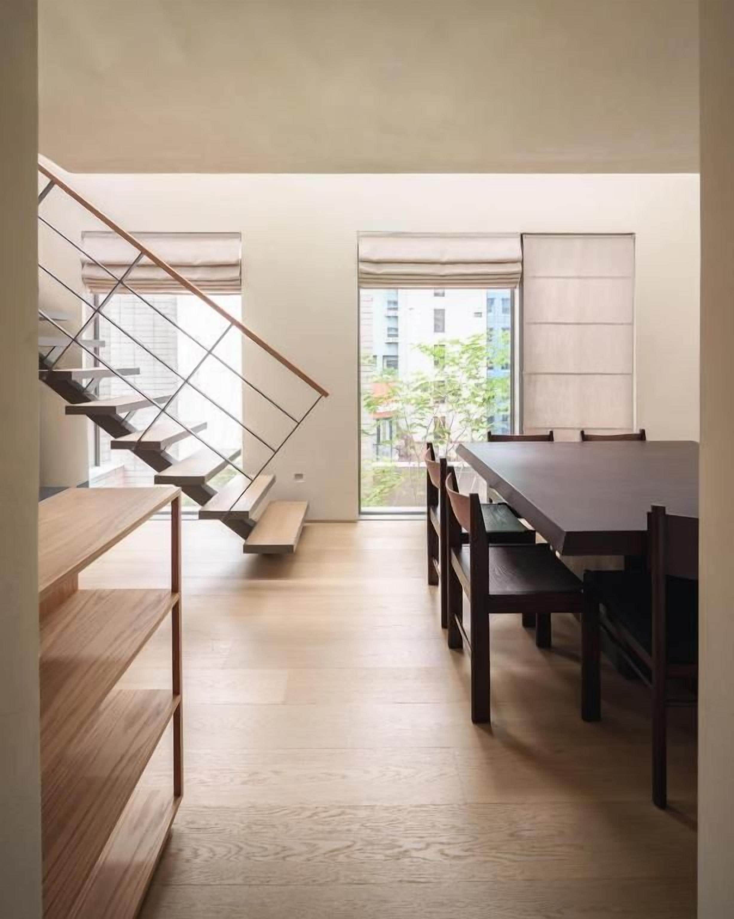 A modern interior with a staircase, a dining table, and a view through a window.