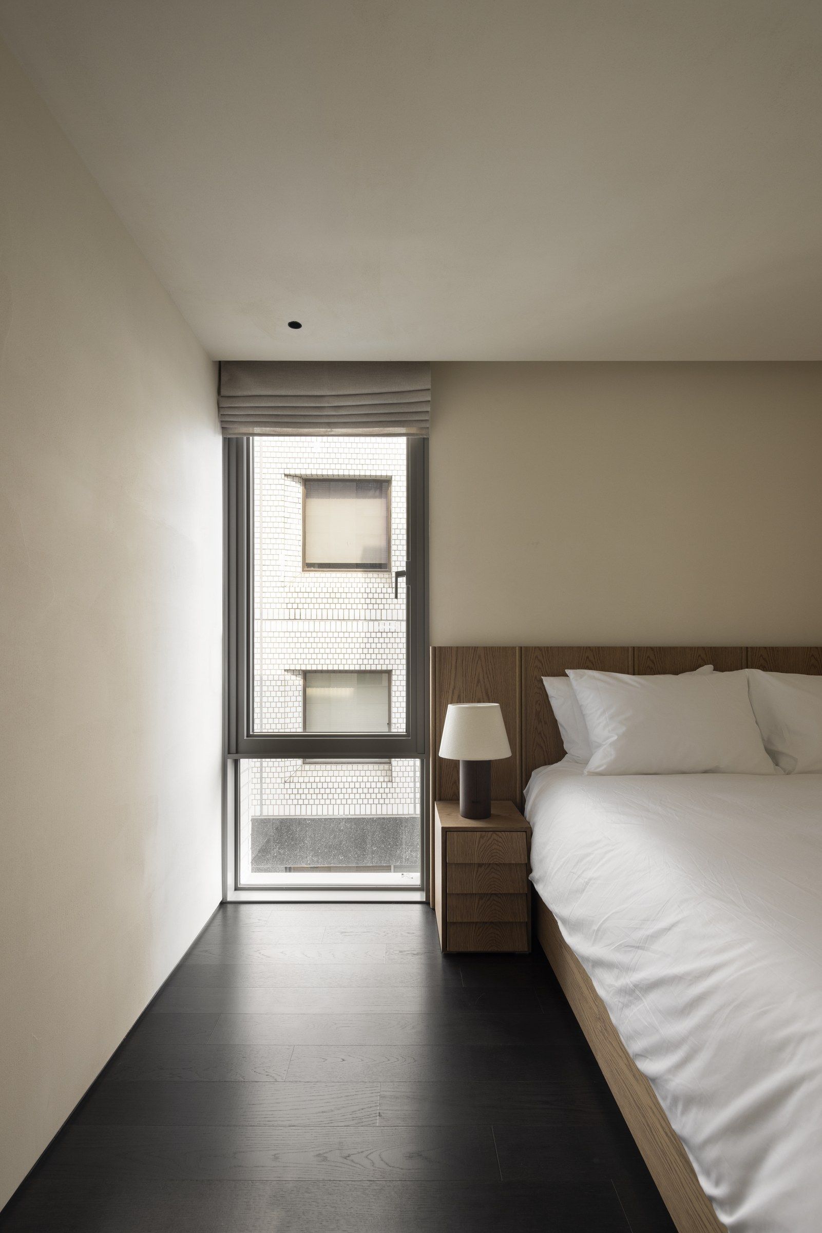 A hotel room with a bed, a nightstand, a lamp, and a window with blinds.