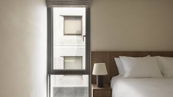 A hotel room with a bed, a nightstand, a lamp, and a window with blinds.