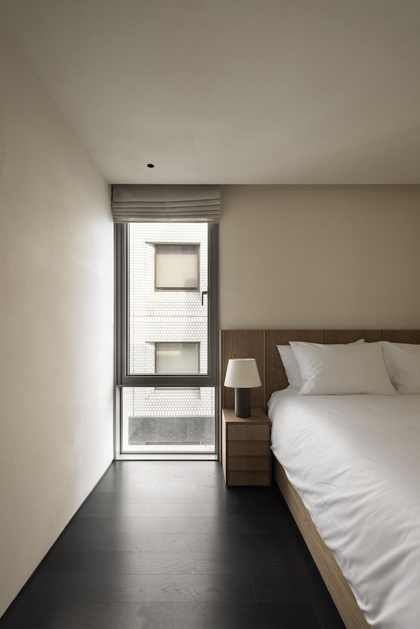 A hotel room with a bed, a nightstand, a lamp, and a window with blinds.