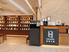 A hotel reception area with a reception desk, a bookshelf with magazines, and a sign indicating the hotel name.