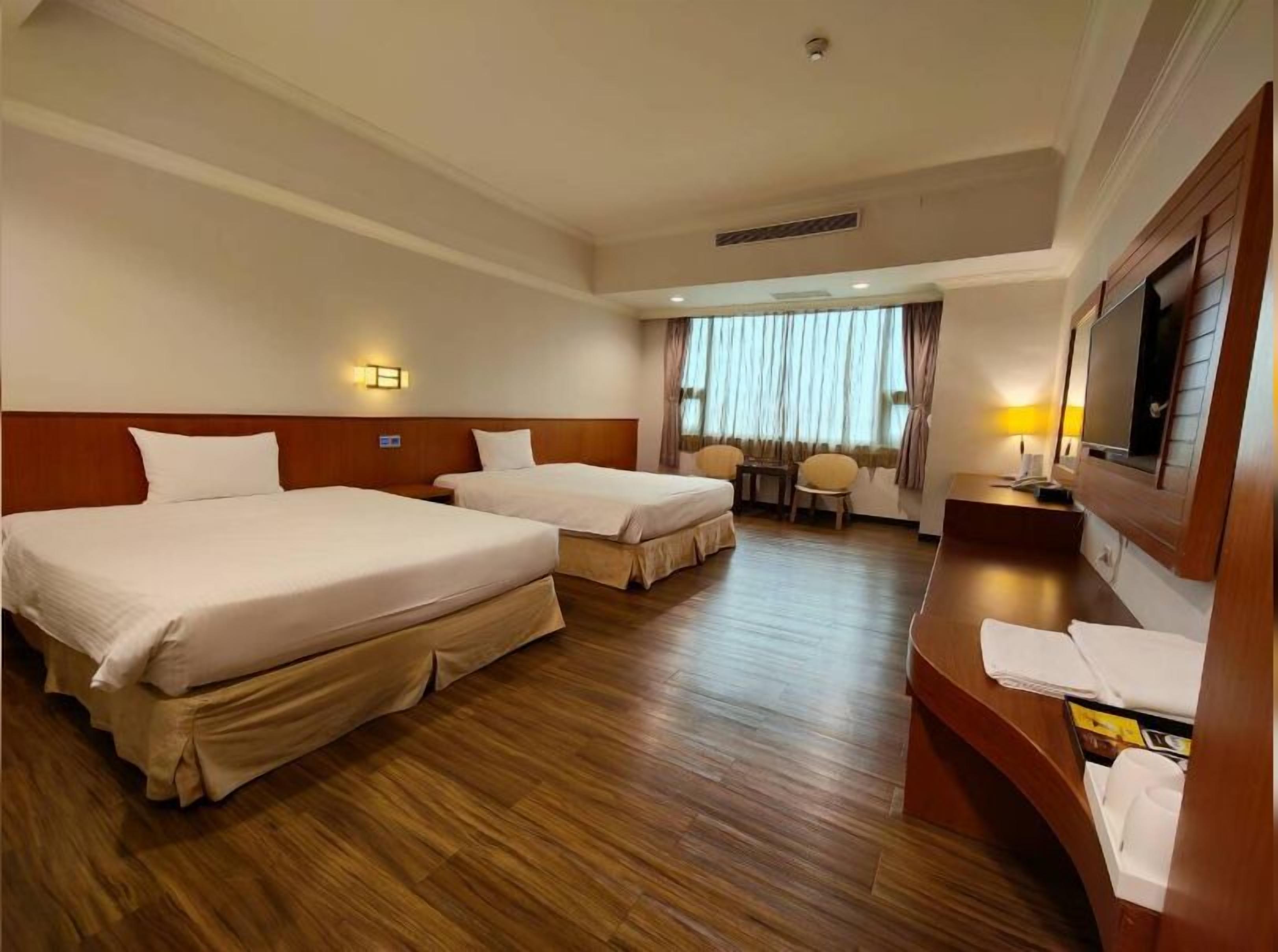 Une chambre d’hôtel avec deux lits, un bureau, une chaise et un téléviseur.