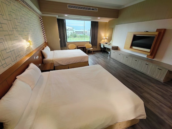A hotel room with two beds, a desk, a chair, a television, and a window with a view of buildings.