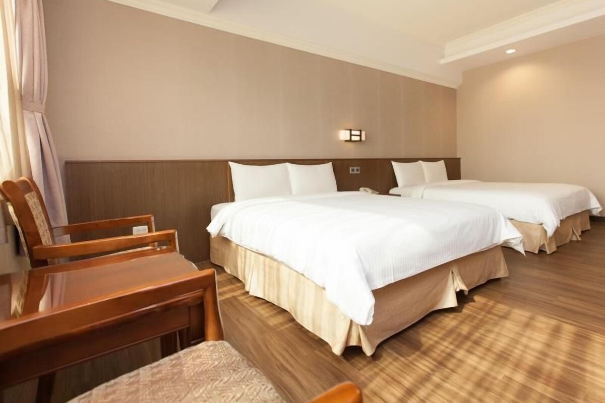 Habitación de hotel con dos camas, un escritorio de madera y una silla.