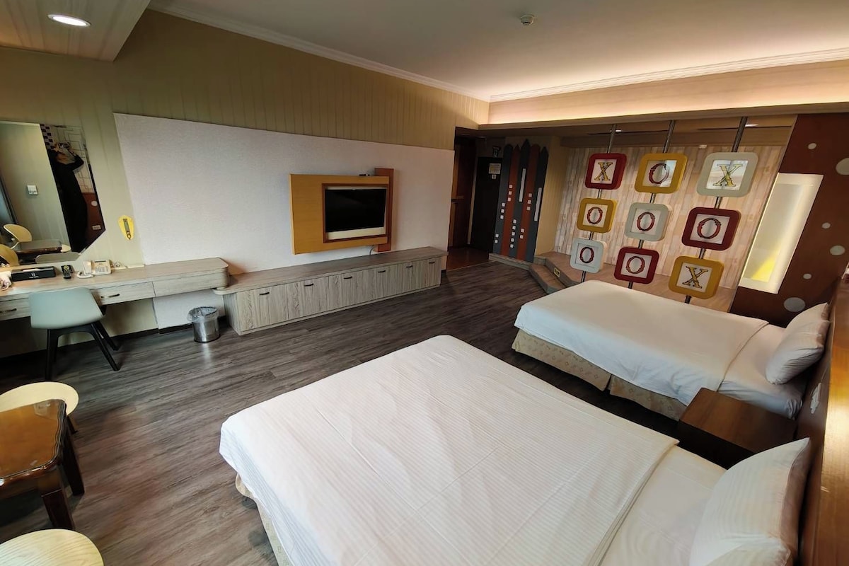 Habitación de hotel con dos camas, un escritorio, un televisor y una pared decorada.