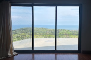 Una habitación con un gran ventanal corredera que da a un balcón con vista al océano y al follaje.