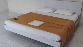 Une chambre avec un lit simple, une tête de lit blanche, une couvre-lit marron et du linge de lit blanc.