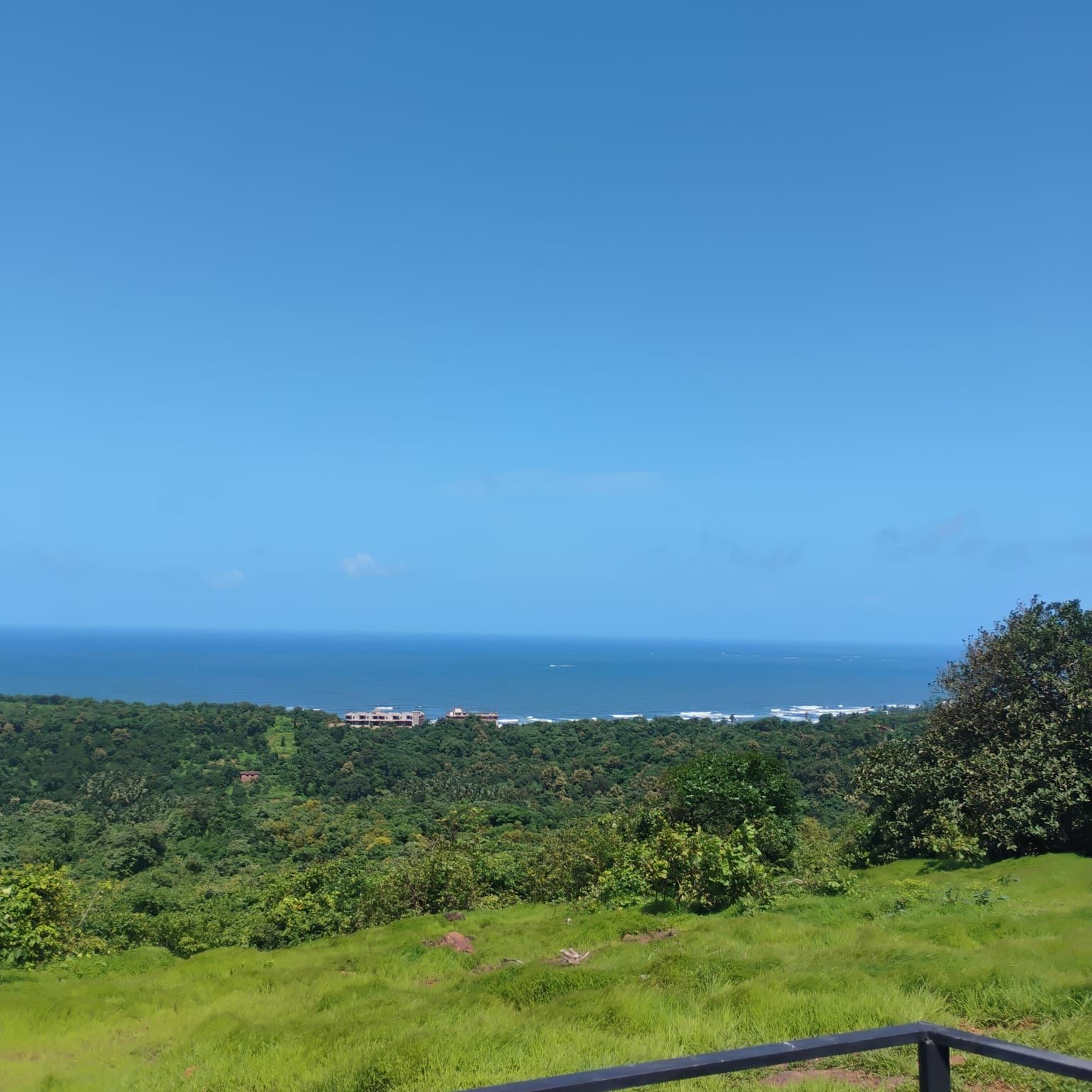 A coastal landscape with a clear view of the ocean and a lush green hillside.