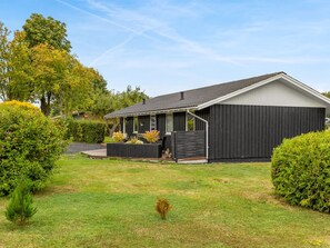 Een gelijkvloers huis met een donkere gevel, een overdekte veranda en een verzorgd gazon.
