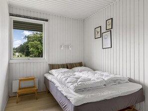 Een slaapkamer met een bed, een raam, een klein tafeltje en wandlampen.