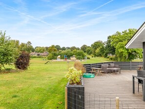 Une terrasse en bois avec des meubles d’extérieur, une pelouse et, au fond, une aire de jeux.