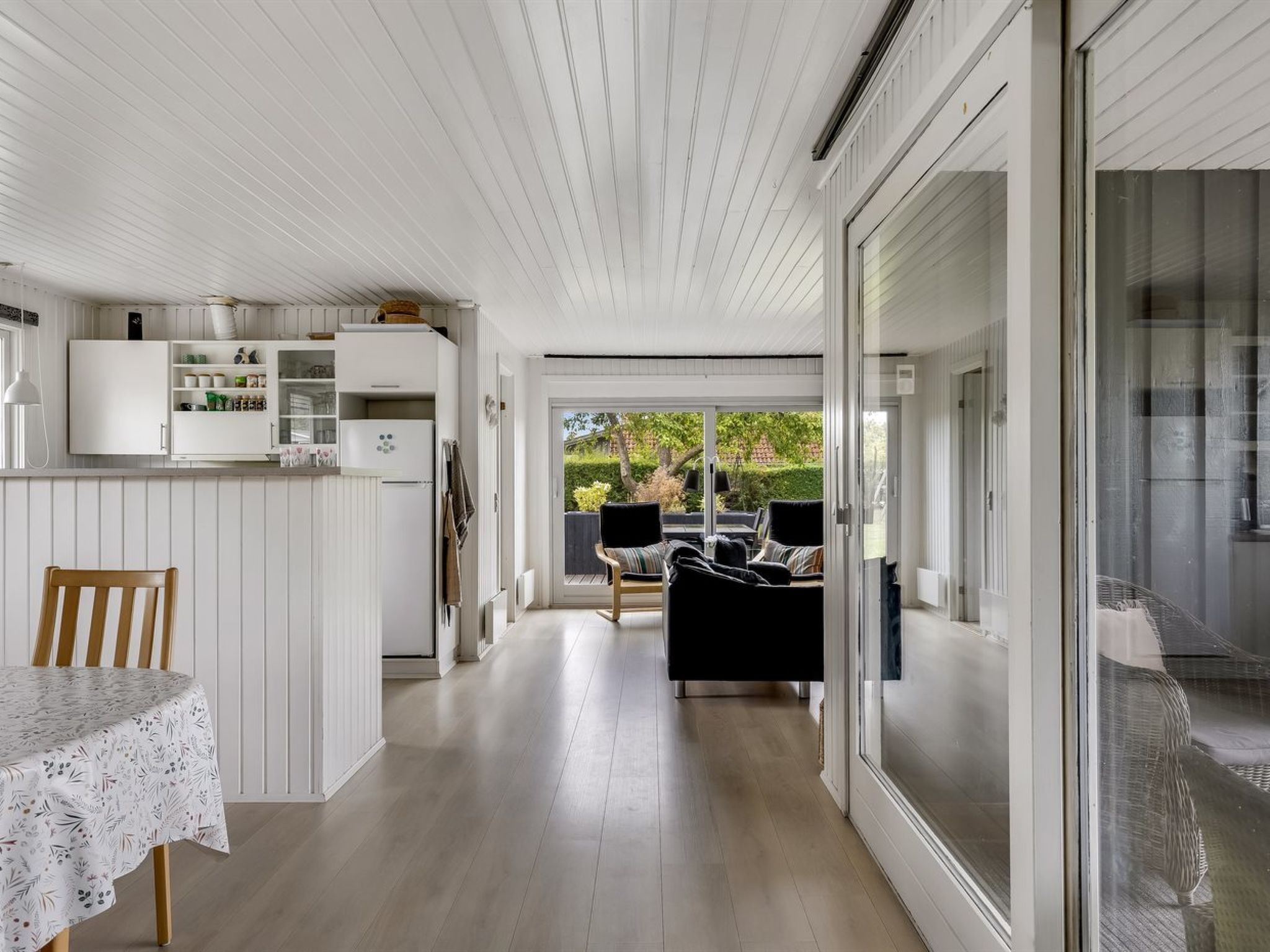 A modern kitchen with white cabinetry, a dining table with a floral tablecloth, and a sliding glass door leading to a patio area with outdoor furniture.
