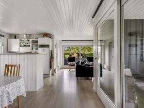 Een moderne keuken met witte kastjes, een eettafel met een tafelkleed met bloemenmotief, en een schuifdeur die leidt naar een terras met buitenmeubilair.