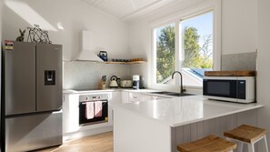A modern kitchen with a refrigerator, stove, oven, microwave, and a window providing a view of trees. - Cascade Canopy Katoomba Mountain Minutes from Three Sisters (Katoomba)