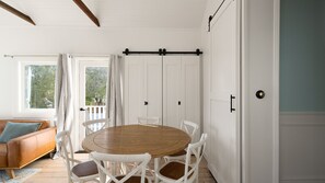A dining area with a round wooden table surrounded by white chairs, a brown leather sofa, and a white door with a black handle. - Cascade Canopy Katoomba Mountain Minutes from Three Sisters (Katoomba)