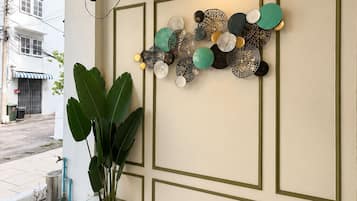 Una habitación con televisión de pantalla plana en la pared, una obra de arte decorativa, una planta grande en maceta y una ventana con vista a la calle.
