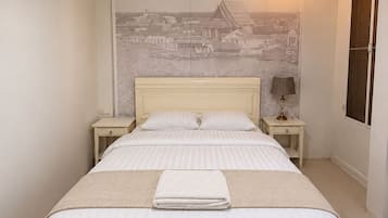 A bedroom with a large bed, two bedside tables, a wall-mounted lamp, and a window with a view of a cityscape.