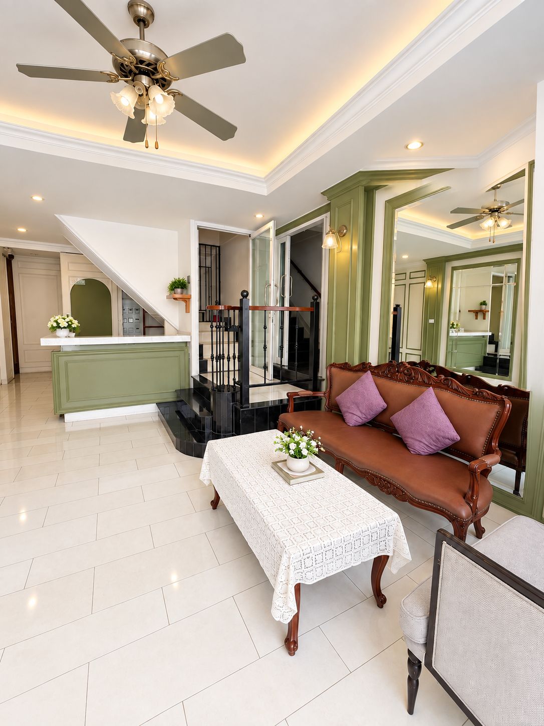 A spacious living room with a high ceiling fan, a brown sofa with purple cushions, a white coffee table with a floral centerpiece, and a staircase leading to an upper level.