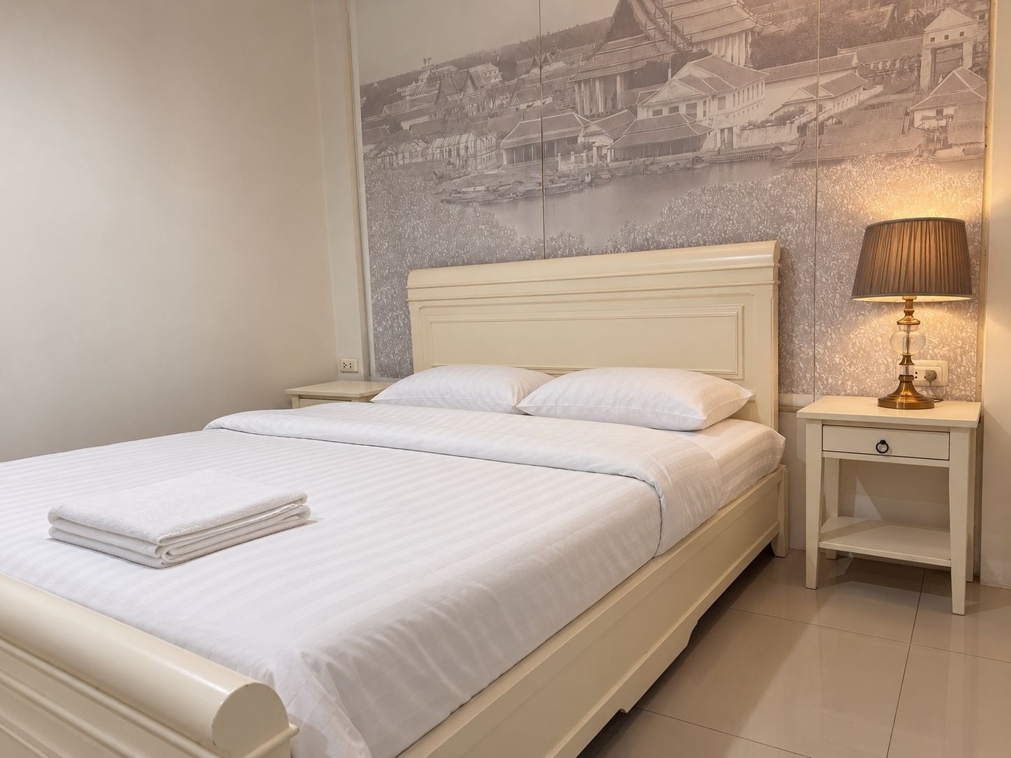 Een hotelkamer met een bed, een nachtkastje met een lamp en een muurschildering.