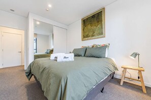 A bedroom with a bed, a bedside lamp, a mirror, and a painting on the wall. - Christchurch CBD - 2BR with Parking & Balcony (Christchurch)