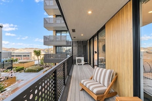 Een balkon met een houten vloer, een comfortabele stoel en een glazen hekwerk.