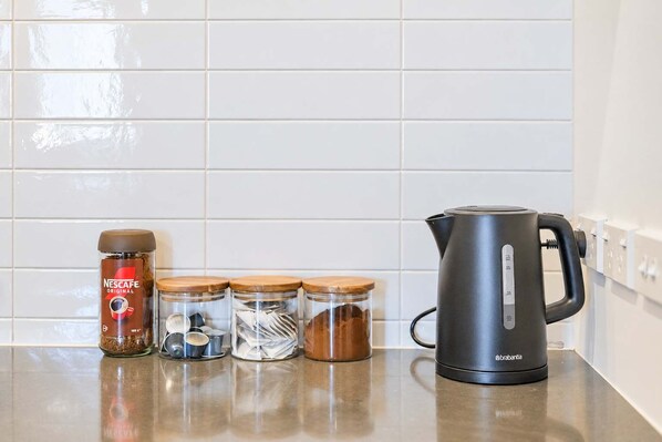 Een keukenblad met een Nescafe Original koffiezetapparaat, drie glazen potten met houten deksels en een zwarte elektrische waterkoker.