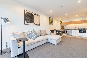 Ein modernes Wohnzimmer mit einem Ecksofa, einem Esstisch und einer kleinen Küchenzeile im Hintergrund.