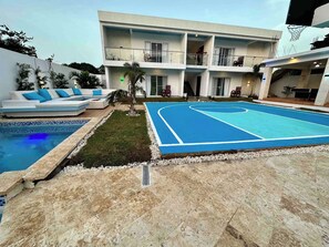 A pool area with a basketball court, a lounge with a sofa, and a building with multiple balconies. - Amazing 12br Villa With 4 Master Rooms (Sosúa)