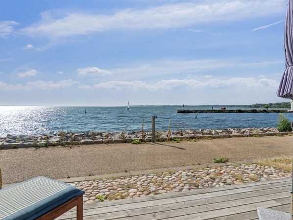 A wooden deck with a view of the sea, a lighthouse, and a rocky shoreline.