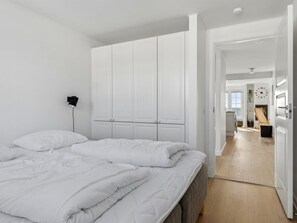 A bedroom with a bed, white wardrobe, and a hallway leading to a living area.