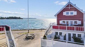 A waterfront property with a red building, a white fence, and a paved area with a table and chairs. - "Loan" - 10m to the fjord by Interhome (Nykøbing Sj)