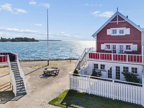 A waterfront property with a red building, a white fence, and a paved area with a table and chairs.