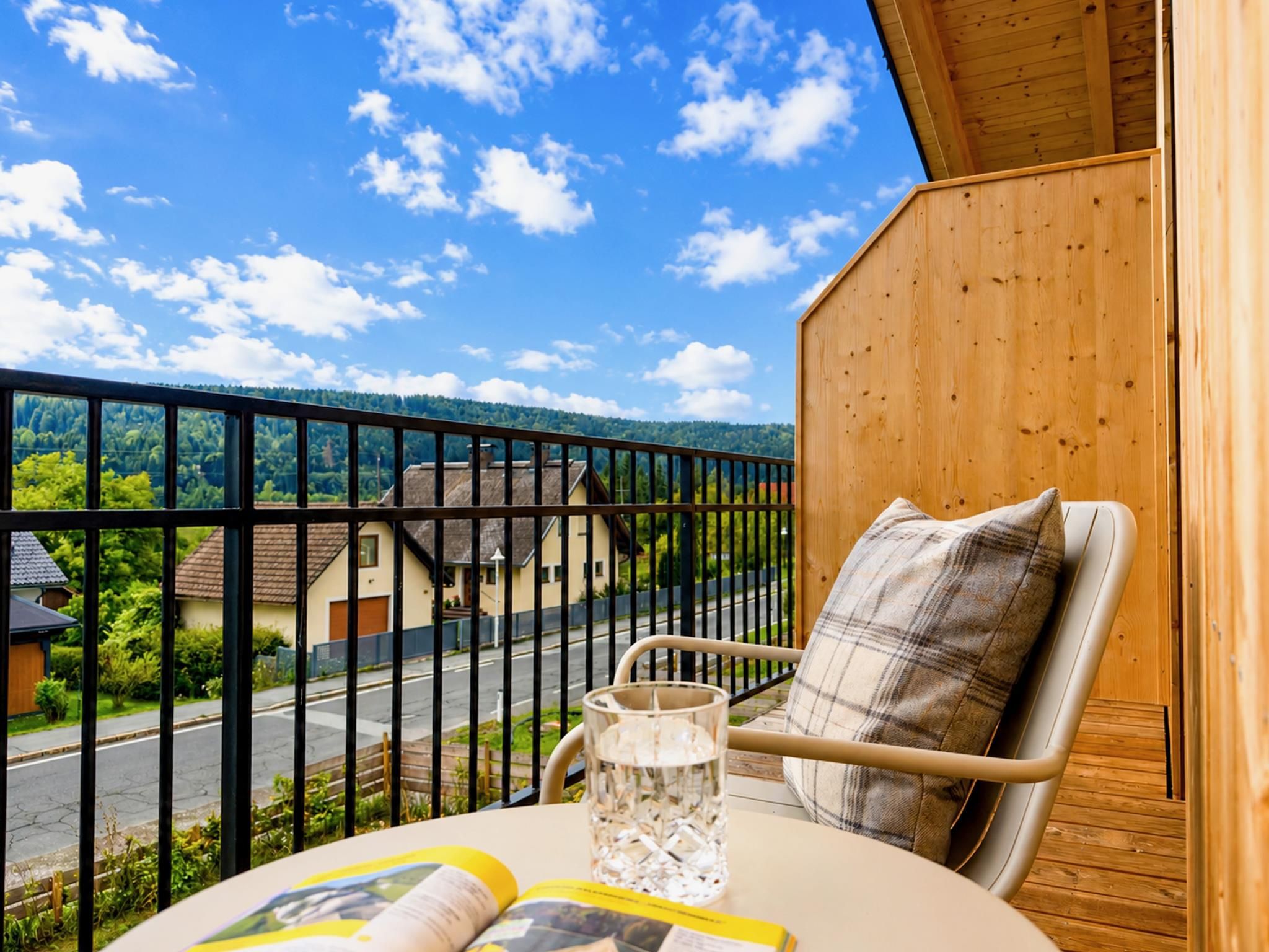 Un balcon donnant sur un quartier résidentiel, une chaise, une table avec un verre et un livre, et un mur en bois.