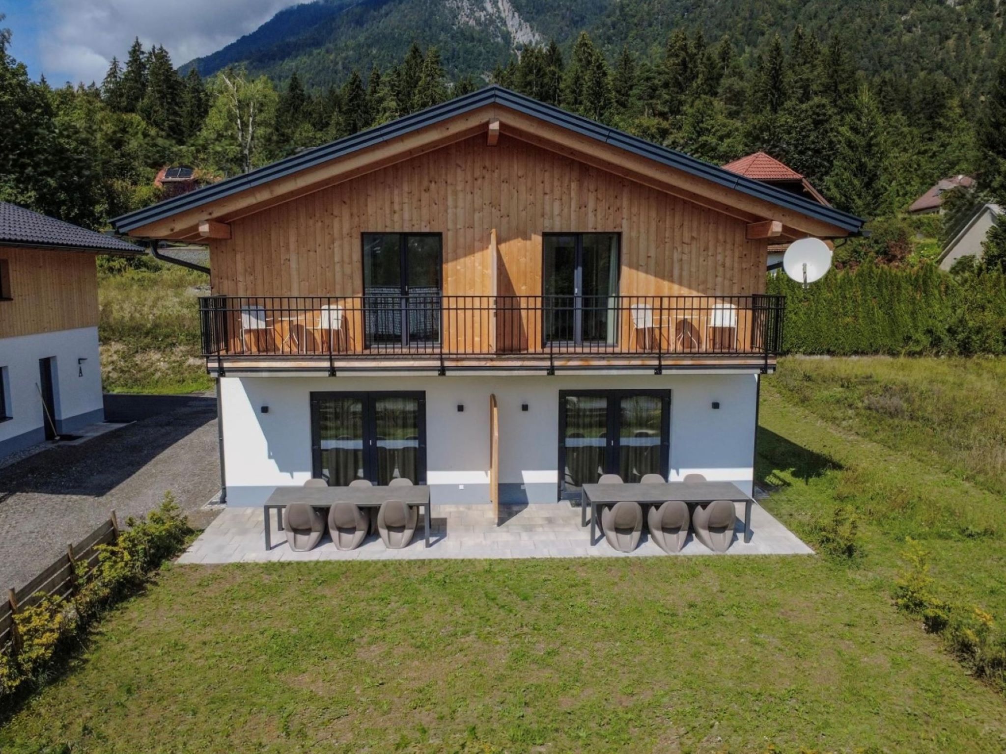 Un chalet en bois à deux étages, doté d’un balcon, d’un espace extérieur aménagé et offrant une vue sur les montagnes.