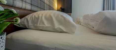 A neatly made bed with white linens and pillows, a lit candle on a bedside table, and a plaid headboard.