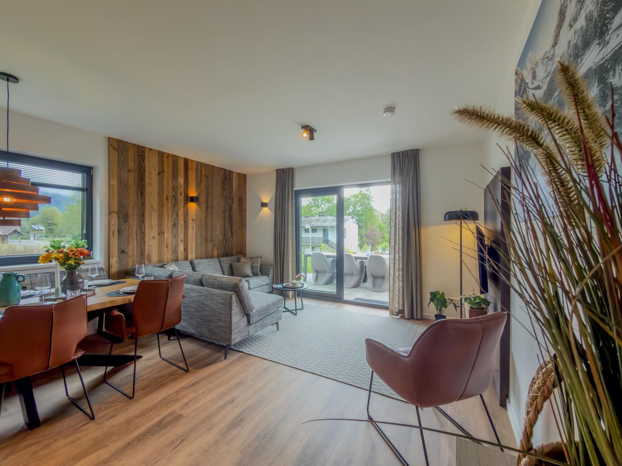 A modern living room with a sofa, dining table, and chairs. There is a large window with a view of the outdoors.