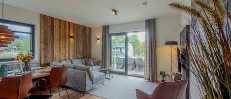 A modern living room with a sofa, dining table, and chairs. There is a large window with a view of the outdoors.