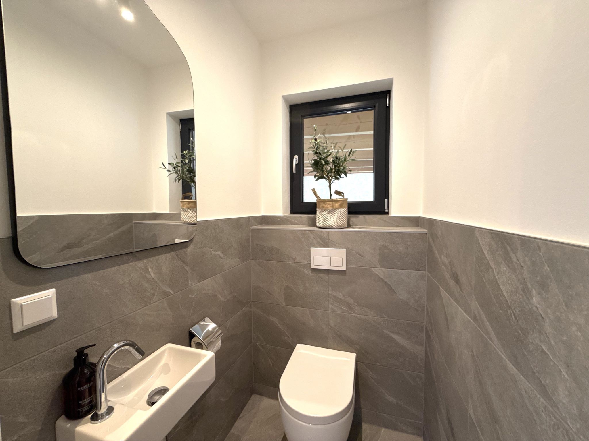 Un bagno moderno con lavandino, WC e una finestra con una pianta.